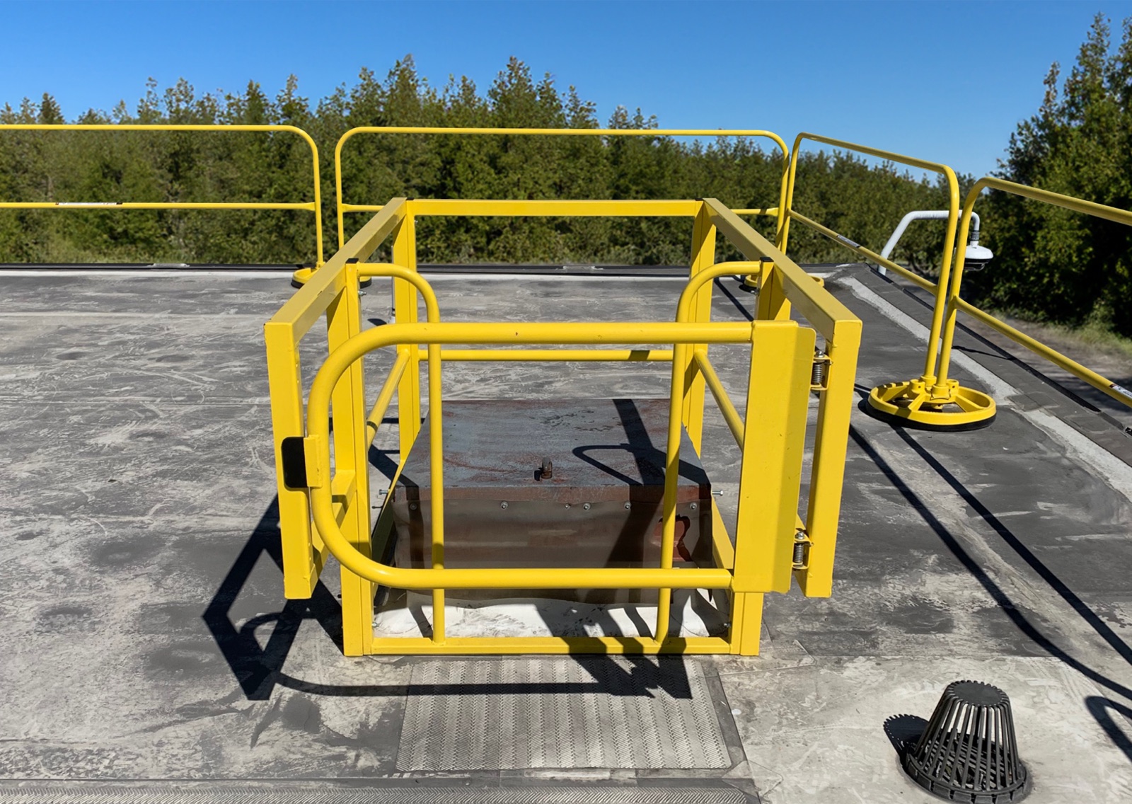 Yellow guardrail and self-closing gate ringing a roof hatch opening on a membrane roof