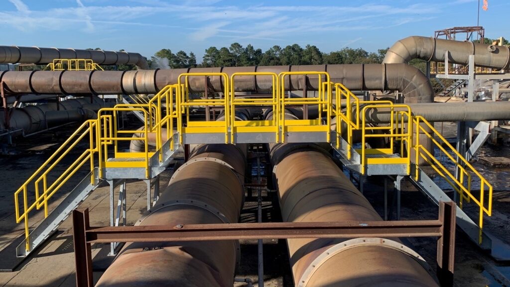 A large modular crossover stair-and-platform system spanning a bank of big process pipes